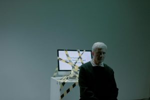 How to Write a Layoff Press Release: Examples & Tips Older man in a dark sweater sitting in front of a computer monitor covered in yellow and black caution tape