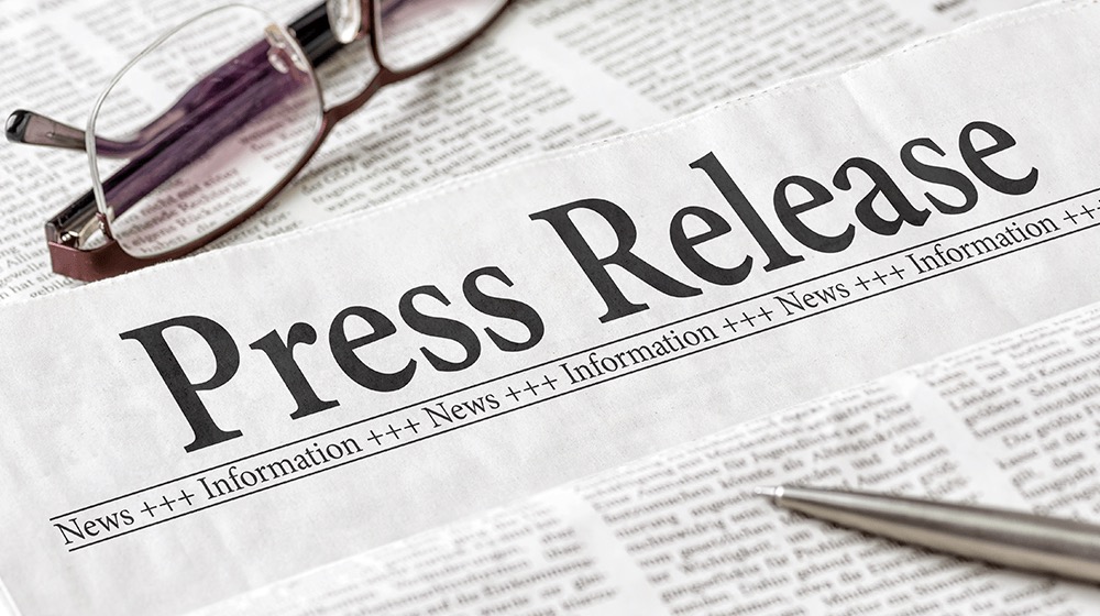Newspaper headline reading "Press Release" with eyeglasses and a silver pen resting on top