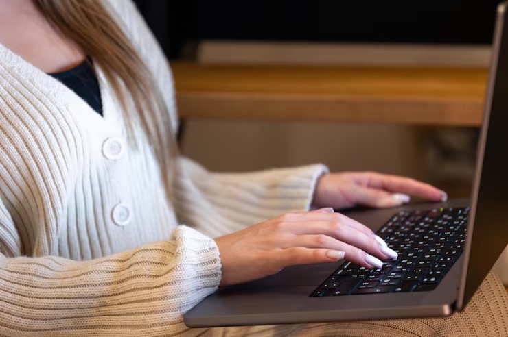 Person in a cream cardigan typing on a laptop keyboard with both hands