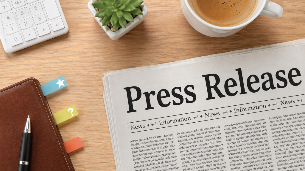 Press release laid out on a wooden desk with a newspaper headline, notebook, pen, and coffee cup.