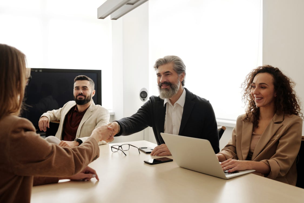 Two executives shaking hands across a boardroom table to mark a new business partnership or collaboration.