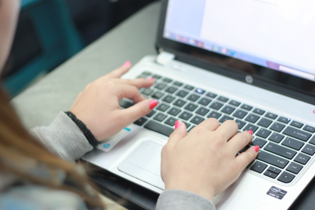 Close-up of hands with pink nail polish typing on a silver HP laptop keyboard.