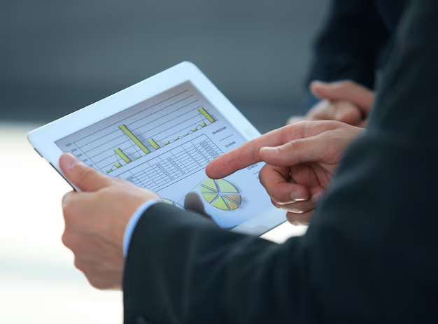 Two businesspeople reviewing financial charts and graphs on a tablet, with one pointing at the data.
