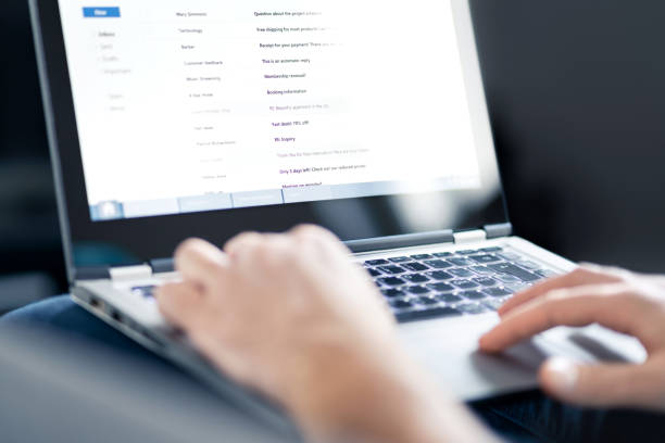 Hands typing on a laptop displaying an email inbox with a list of messages.