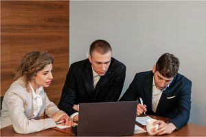 Three colleagues in business attire collaborating around a laptop at a conference table